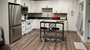 A modern kitchen with white cabinets, stainless steel appliances, a wooden floor, and a central island with bar stools. - New 1 bedroom Sooke oceanfront guest suite  (Sooke)