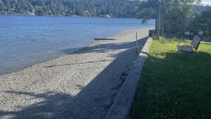 A pebbled beach with a bench and a lamppost, overlooking a calm lake with a forested hillside in the background. - New 1 bedroom Sooke oceanfront guest suite  (Sooke)