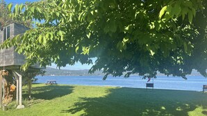 A grassy area with a wooden deck, a bench, and a picnic table by a lake. - New 1 bedroom Sooke oceanfront guest suite  (Sooke)