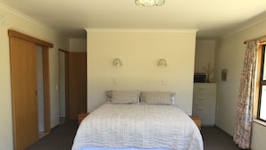 Quarto com cama, duas mesas de cabeceira, guarda-roupa, cômoda e janela com cortinas.