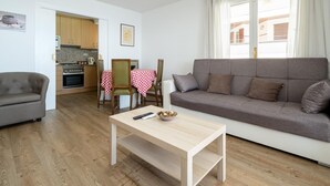 Een woonkamer met een grijze bank, een houten salontafel en een eethoek met een rood-wit geruit tafelkleed.