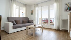 Een moderne woonkamer met een grijze bank, een houten salontafel en een balkon met een tafel en stoelen.