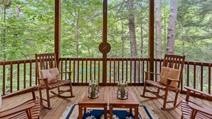 A wooden deck with rocking chairs and a table, surrounded by a wooden railing, overlooking a forest. - Large Luxury Home w/Hot Tub & Game Room with access to Rumbling Bald Resort (Lake Lure)