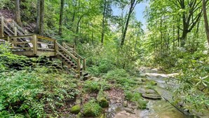 A wooden staircase leading down to a stream in a forested area. - Large Luxury Home w/Hot Tub & Game Room with access to Rumbling Bald Resort (Lake Lure)