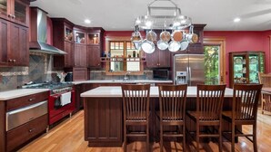 A spacious kitchen with dark wooden cabinets, a central island with bar stools, and a stainless steel refrigerator. - Large Luxury Home w/Hot Tub & Game Room with access to Rumbling Bald Resort (Lake Lure)