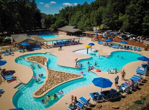 Una piscina con varias pistas de natación y una zona poco profunda separada, rodeada de sillones de descanso y sombrillas.