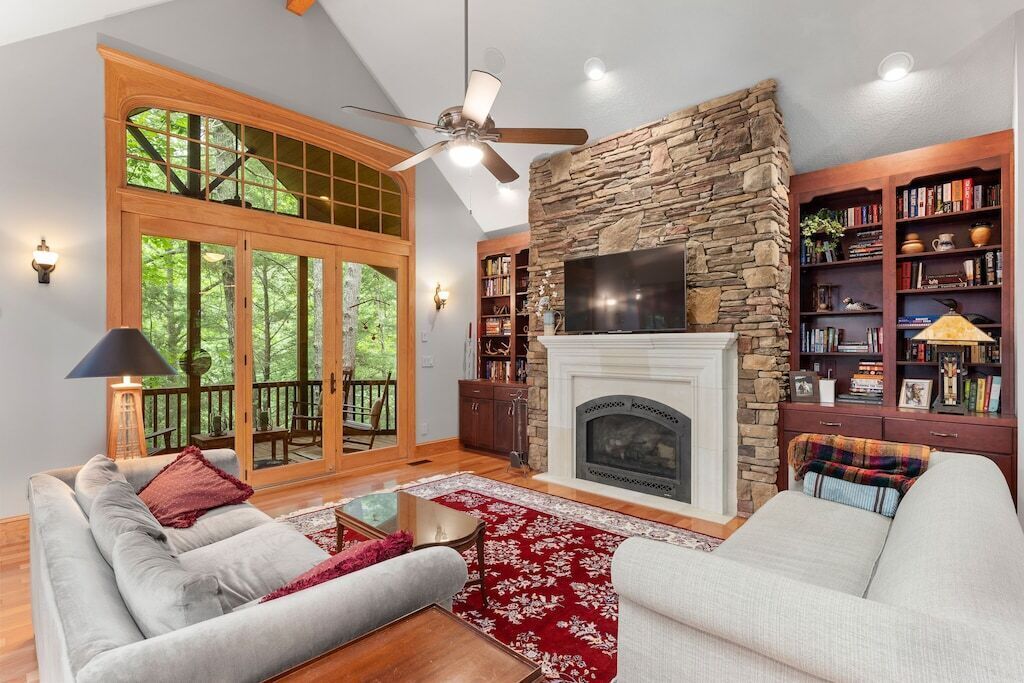 A spacious living room with a stone fireplace, a large TV, and a bookshelf filled with books.
