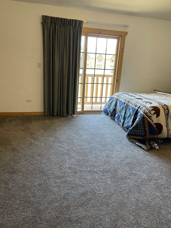 A bedroom with a large window, a bed with a patterned bedspread, and a carpeted floor.