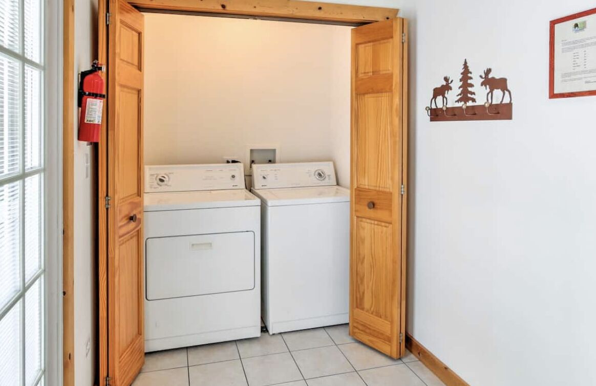 A laundry room with two stacked washers and dryers, wooden doors, a fire extinguisher, and a certificate on the wall.