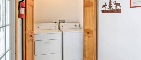 A laundry room with two stacked washers and dryers, wooden doors, a fire extinguisher, and a certificate on the wall.