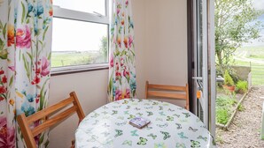 Una habitación con una mesa redonda, dos sillas y vistas a un paisaje rural a través de una ventana con cortinas florales.