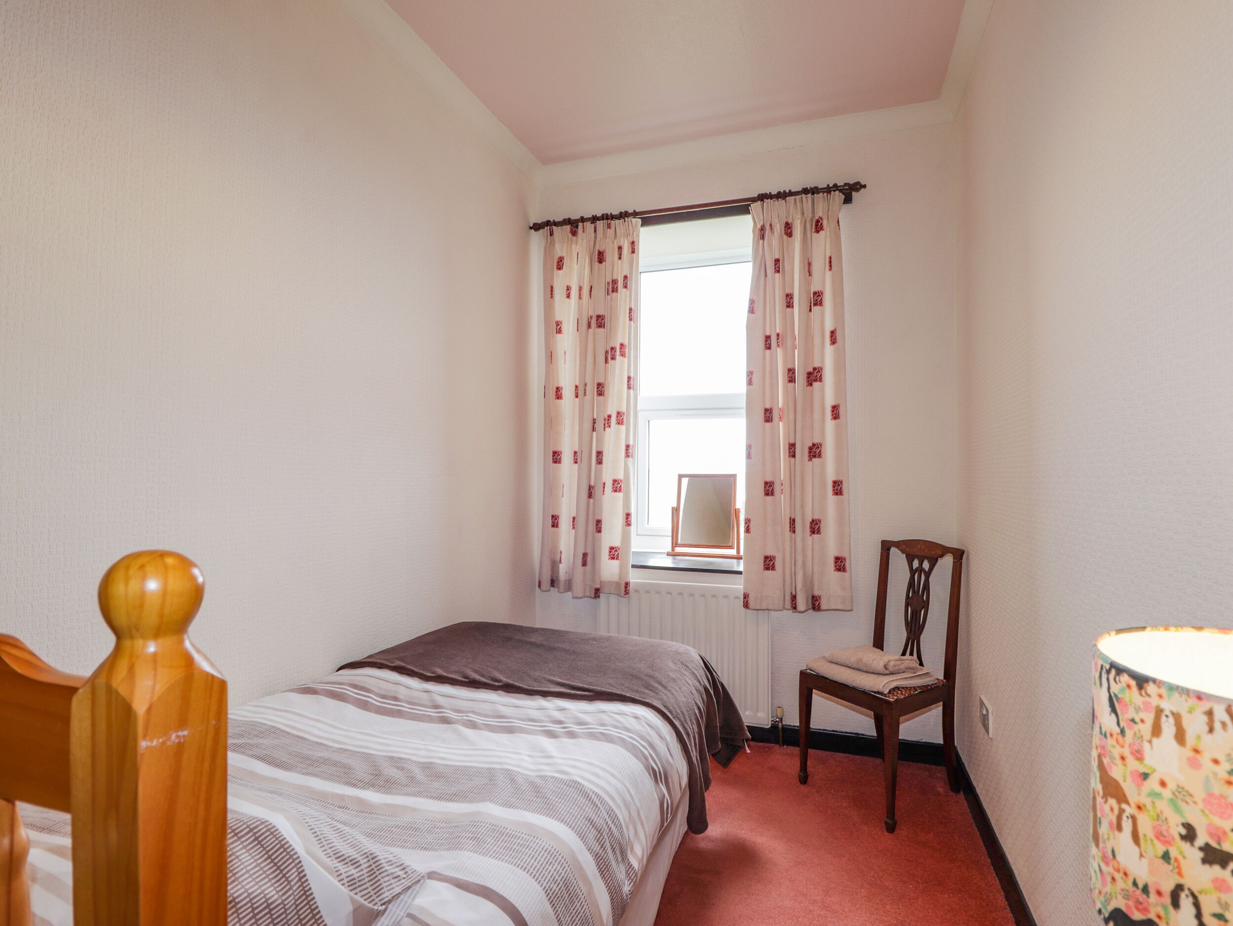 A bedroom with a bed, a chair, a lamp, and a window with curtains.