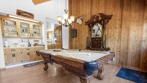 Una mesa de billar en una sala con paneles de madera, un mueble de madera con puertas de cristal y un espejo con marco decorativo.