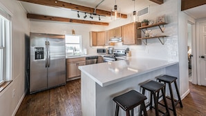 A modern kitchen with wooden beams, a large island with stools, stainless steel appliances, and pendant lighting. - The Surfsonian - 2nd Row Beach House - Dog Friendly - Ocean View (Freeport)