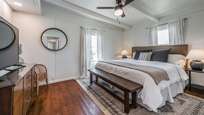 A bedroom with a bed, bedside tables, a ceiling fan, a mirror, and a wooden bench. - The Surfsonian - 2nd Row Beach House - Dog Friendly - Ocean View (Freeport)