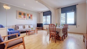 Een moderne woonkamer met een bank, een eettafel voor vier personen, een televisie en kunst aan de muur.