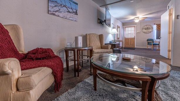 En stue med en beige sofa, et rødt plaide, et glas-sofabord og et billede på væggen.