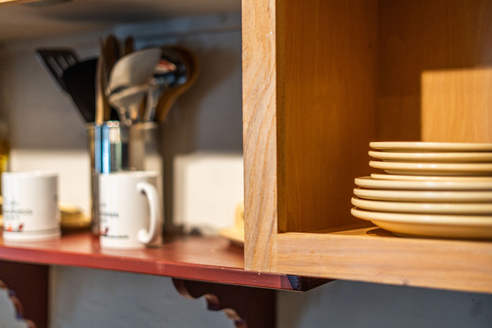 A kitchen shelf with white mugs, a knife block, and stacked plates.