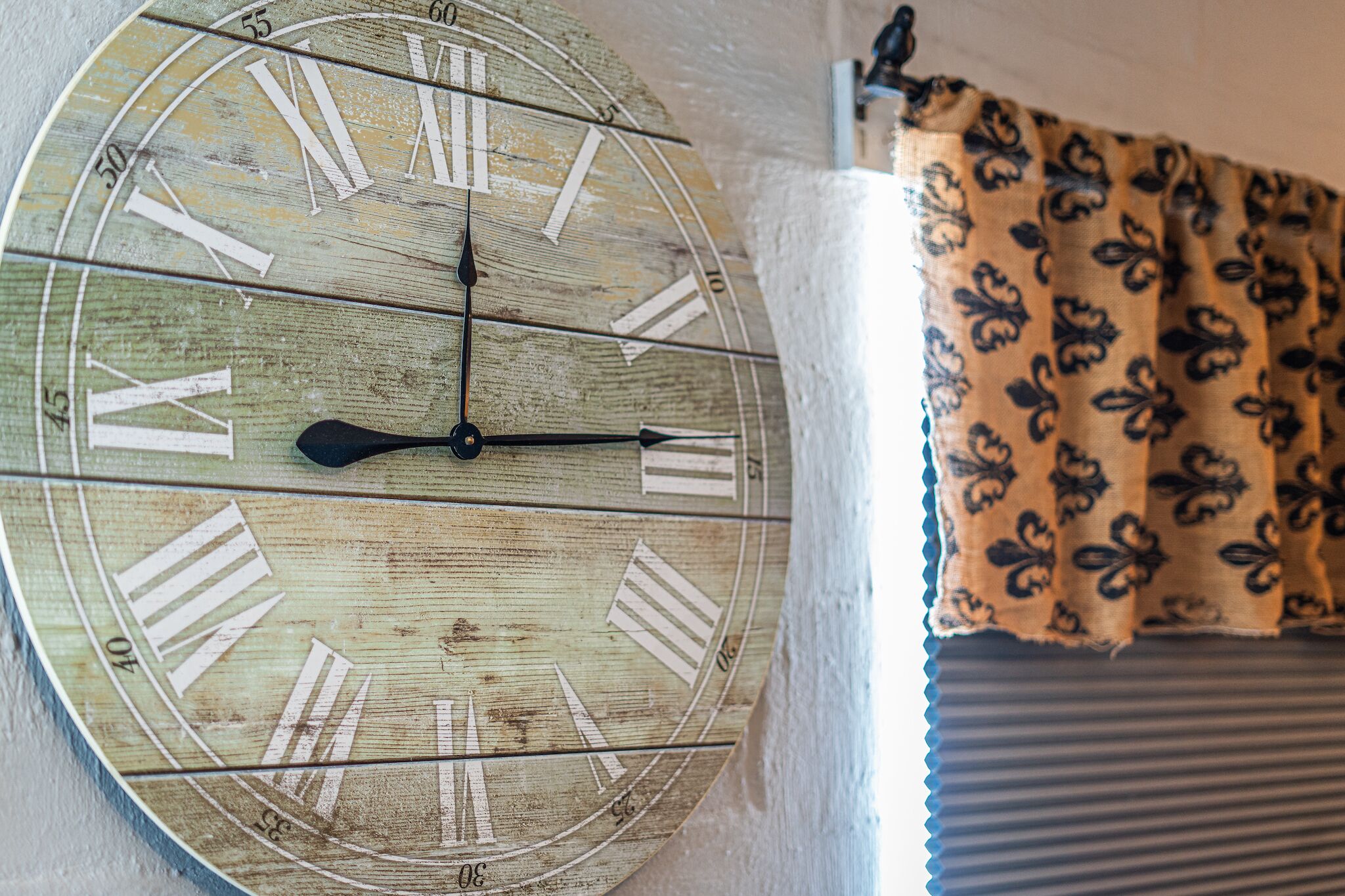 Une horloge murale en bois avec des chiffres romains et un rideau à motifs.
