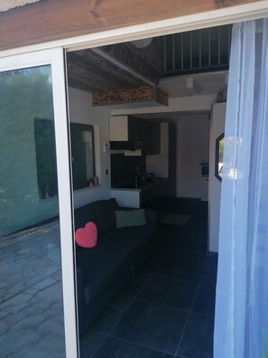 A modern living area with a dark sofa, a small kitchen, and a glass door leading outside.