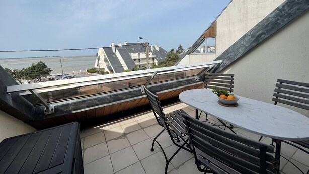 A balcony with a table and chairs, overlooking a body of water and buildings. - Apartment with direct view of the Bay of the Somme (Le Crotoy)