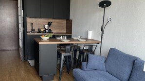 A modern living room with a blue sofa, a white coffee table, and a kitchen area with a dining table and chairs. - Apartment with direct view of the Bay of the Somme (Le Crotoy)