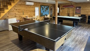 Et værelse med pingpongbord, billardbord, trævægge, en trappe og et køleskab.