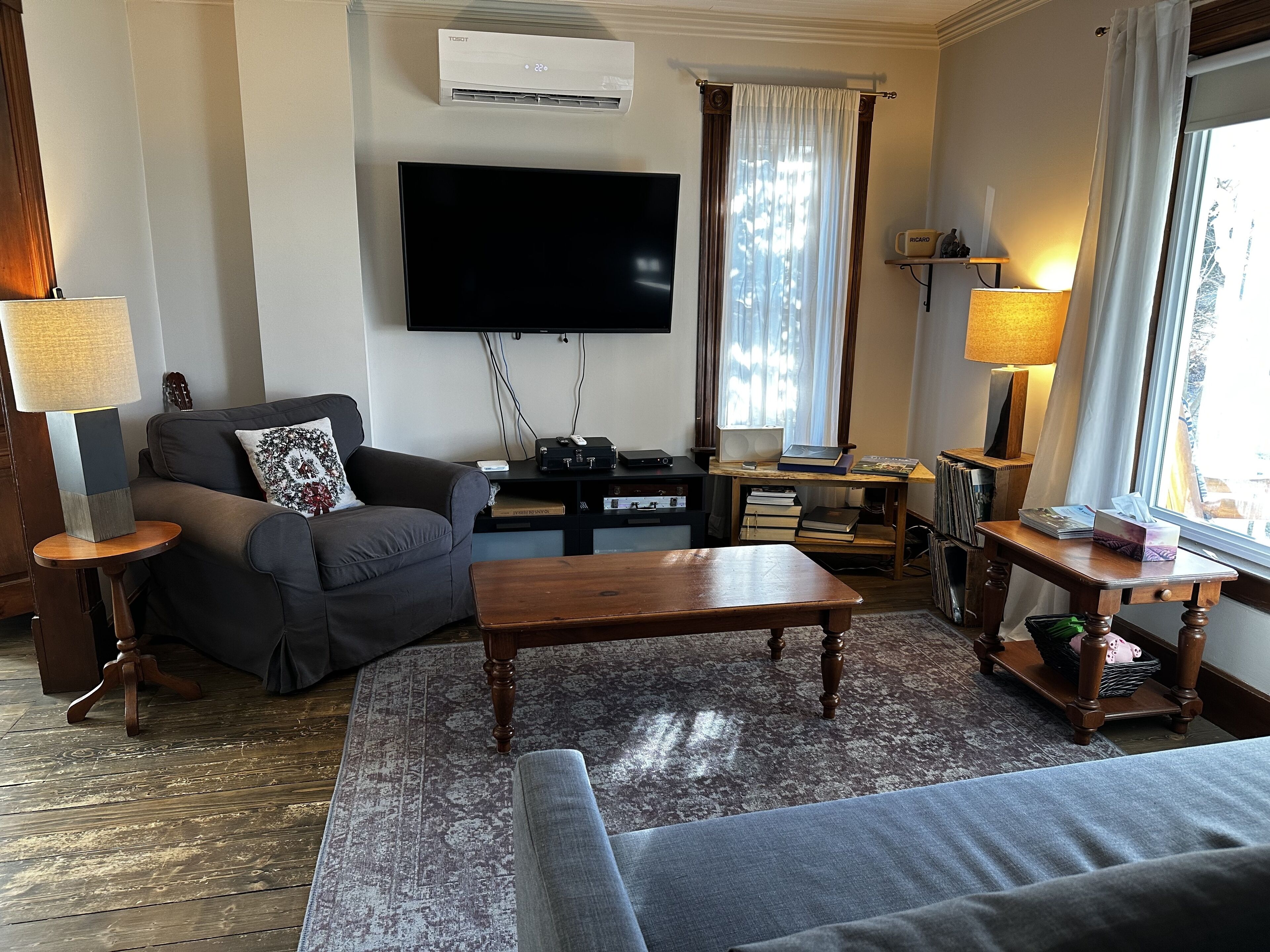 Una sala de estar con sofá, mesa de centro, televisor de pantalla plana, lámpara y ventana con cortinas.
