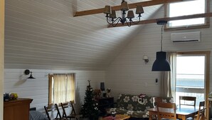 Et hyggeligt værelse i sommerhusstil med en hems, et træbord, en lille juletræ og et stort vindue.