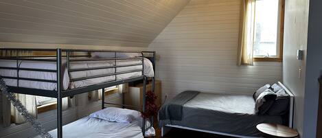 Una habitació de dormitori amb llits superposats, una taula petita i una finestra amb cortines.