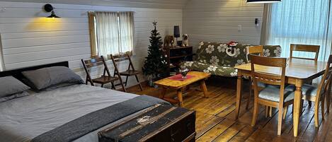 A cozy room with a bed, wooden chairs, a small table, a Christmas tree, and a dining table with chairs.