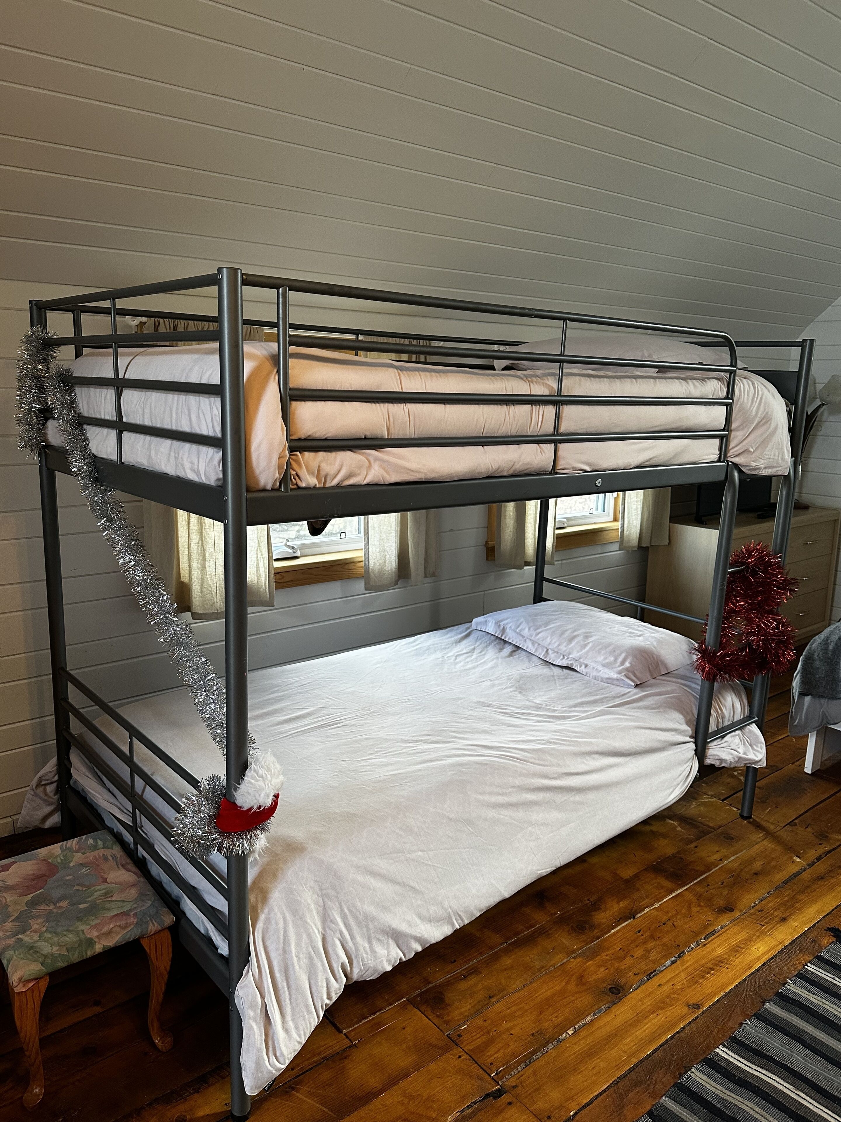 A bunk bed with white bedding, a wooden bench, and a red and silver tinsel decoration.