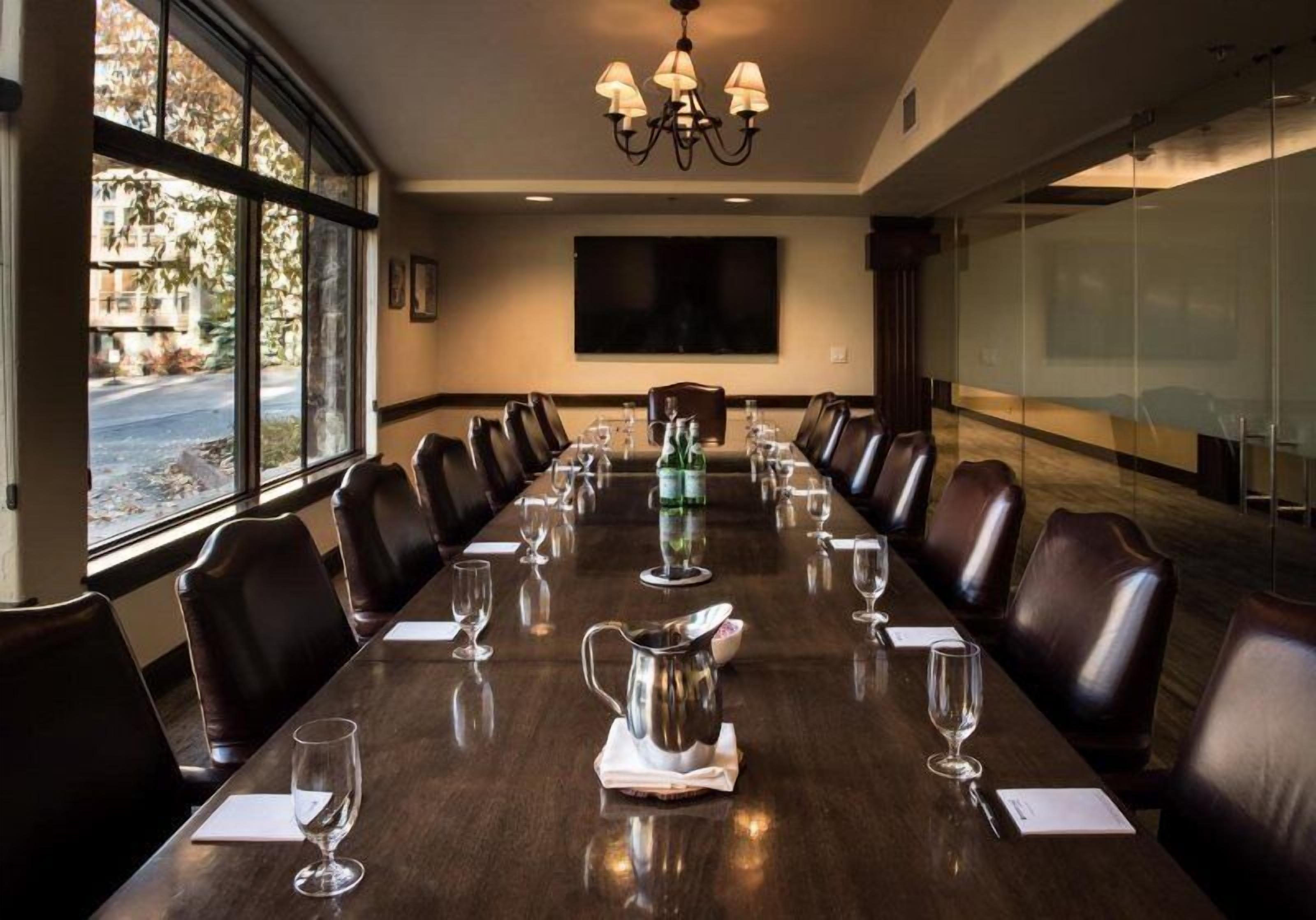 A conference room with a long table, leather chairs, a chandelier, and large windows.