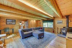 A cozy cabin interior with a large L-shaped gray sofa, a dining table with chairs, a fireplace, and wooden walls. - Historic Century-Old Cabin in Downtown Hope (Hope)