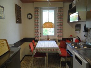 A compact kitchen with a dining table, chairs, a stove, and a window with curtains. - Sunnmatt Süd Wohnung 246 Appartement/Fewo 4-Bettwohnung by Interhome (Engelberg)