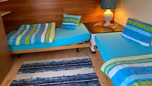 A room with two beds, a wooden wall, a lamp, and a rug.