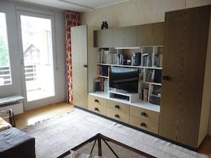 A living room with a television, bookshelf, and a sliding door to a balcony. - Sunnmatt Süd Wohnung 246 Appartement/Fewo 4-Bettwohnung by Interhome (Engelberg)