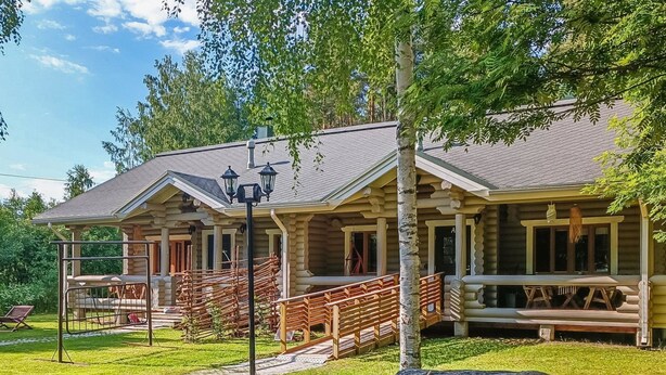 Une cabane en rondins dotée d’un porche, d’un espace extérieur couvert aménagé en salon et d’un chemin en pierre menant à l’entrée.