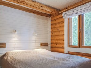 A bedroom with a bed, wooden walls, a window with curtains, and two wall-mounted lights.