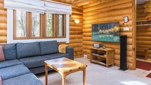 L’intérieur d’une cabane en rondins, avec un canapé, une table basse, un téléviseur et un tableau représentant une forêt.