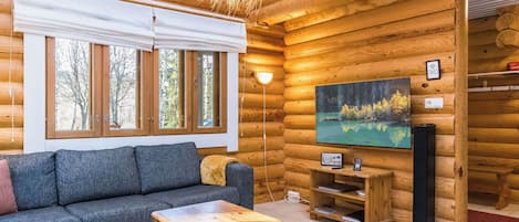 Interior de cabana de tronco com sofá, mesa de centro, televisão e pintura de uma floresta.