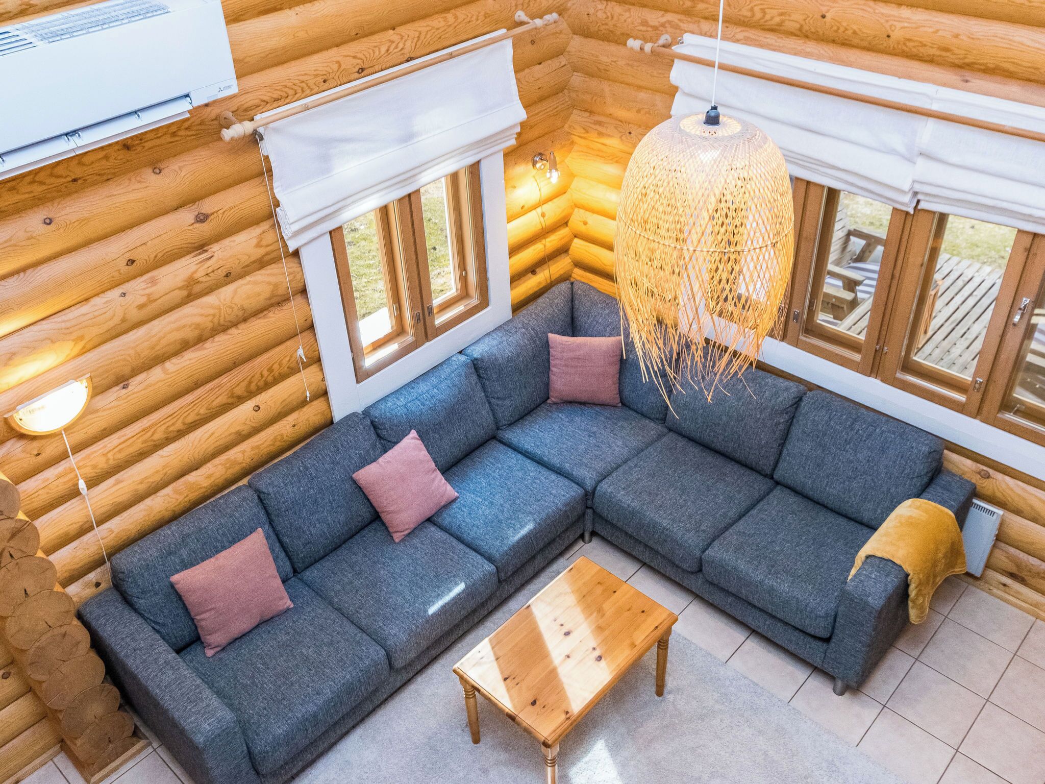A log cabin interior with a sectional sofa, a wooden coffee table, and a hanging light fixture.