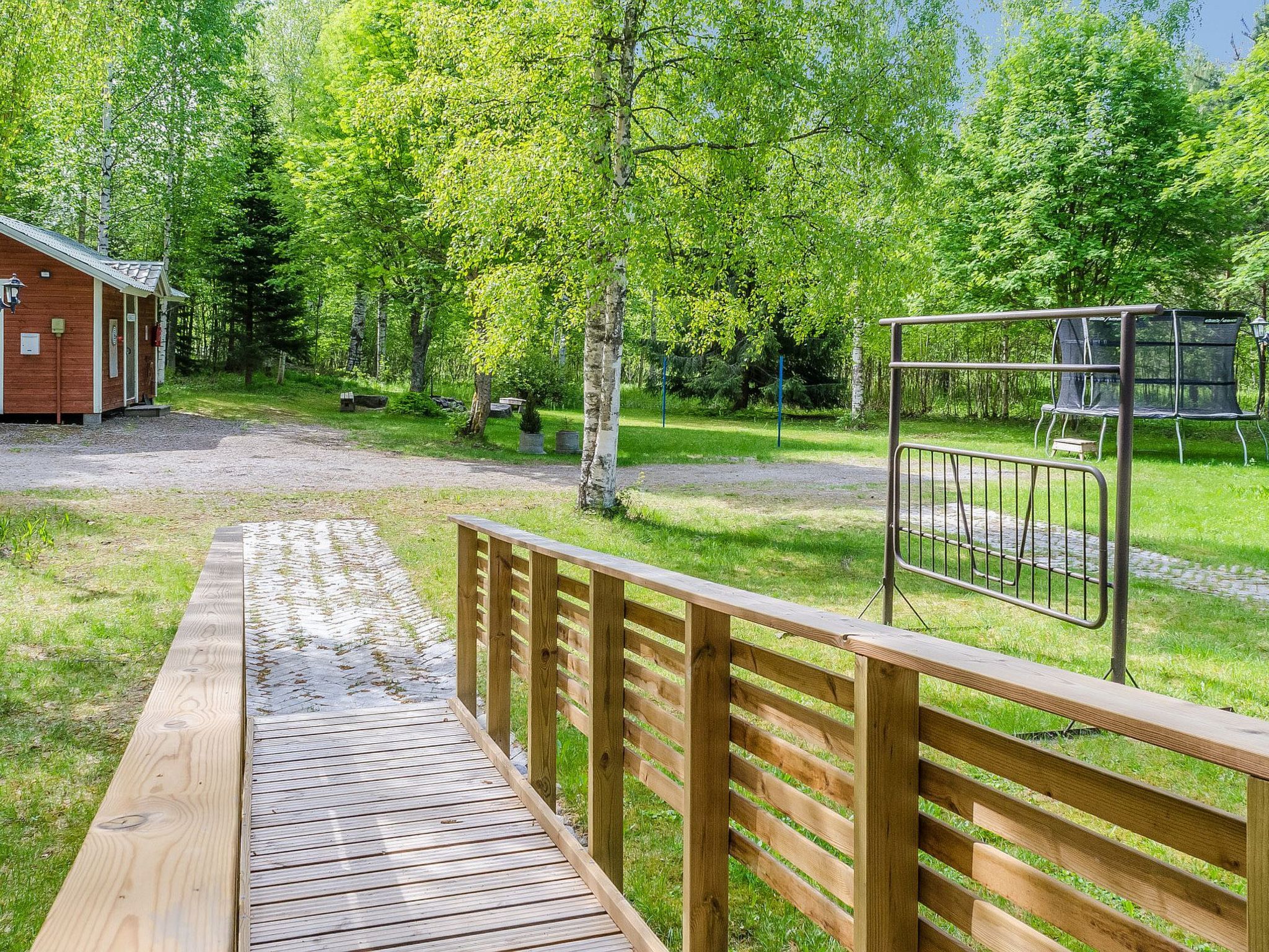 A wooden deck leading to a fenced area with a bench and a small building.