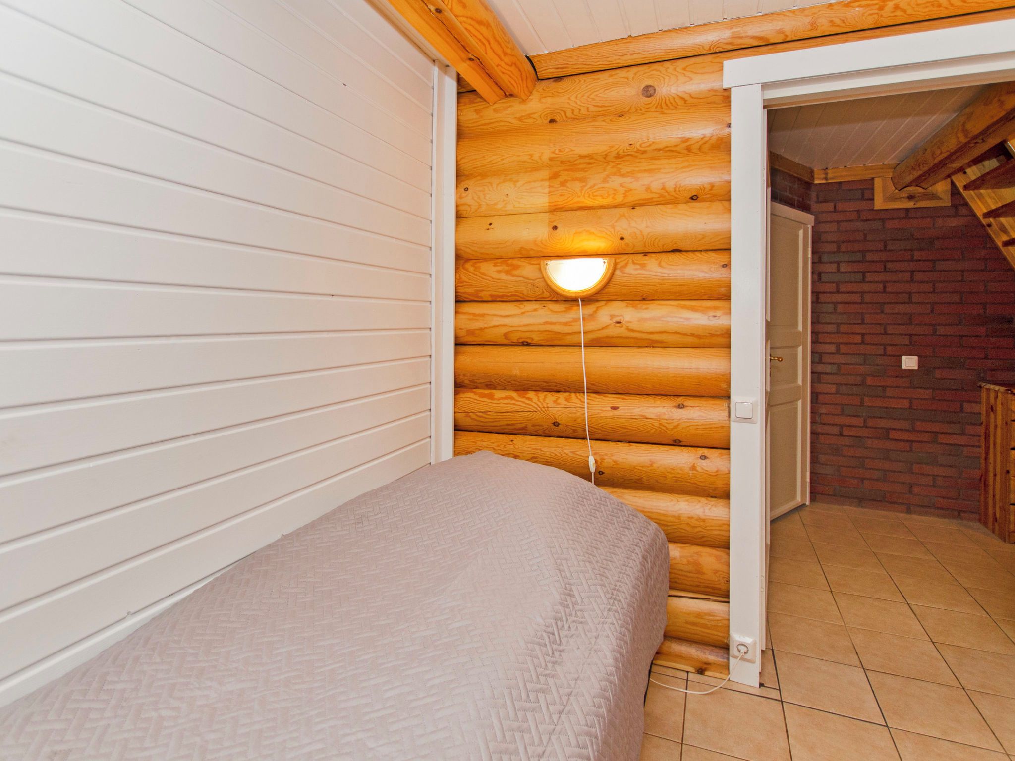 Een slaapkamer met een bed, houten wand, een deur en een lamp.