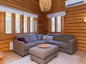 A log cabin interior with a sectional sofa, a small ottoman, and large windows.