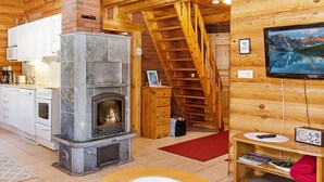 A cozy cabin interior with a stone fireplace, wooden staircase, kitchen area, and a mounted television. - Purnutar b by Interhome (Lieksa)