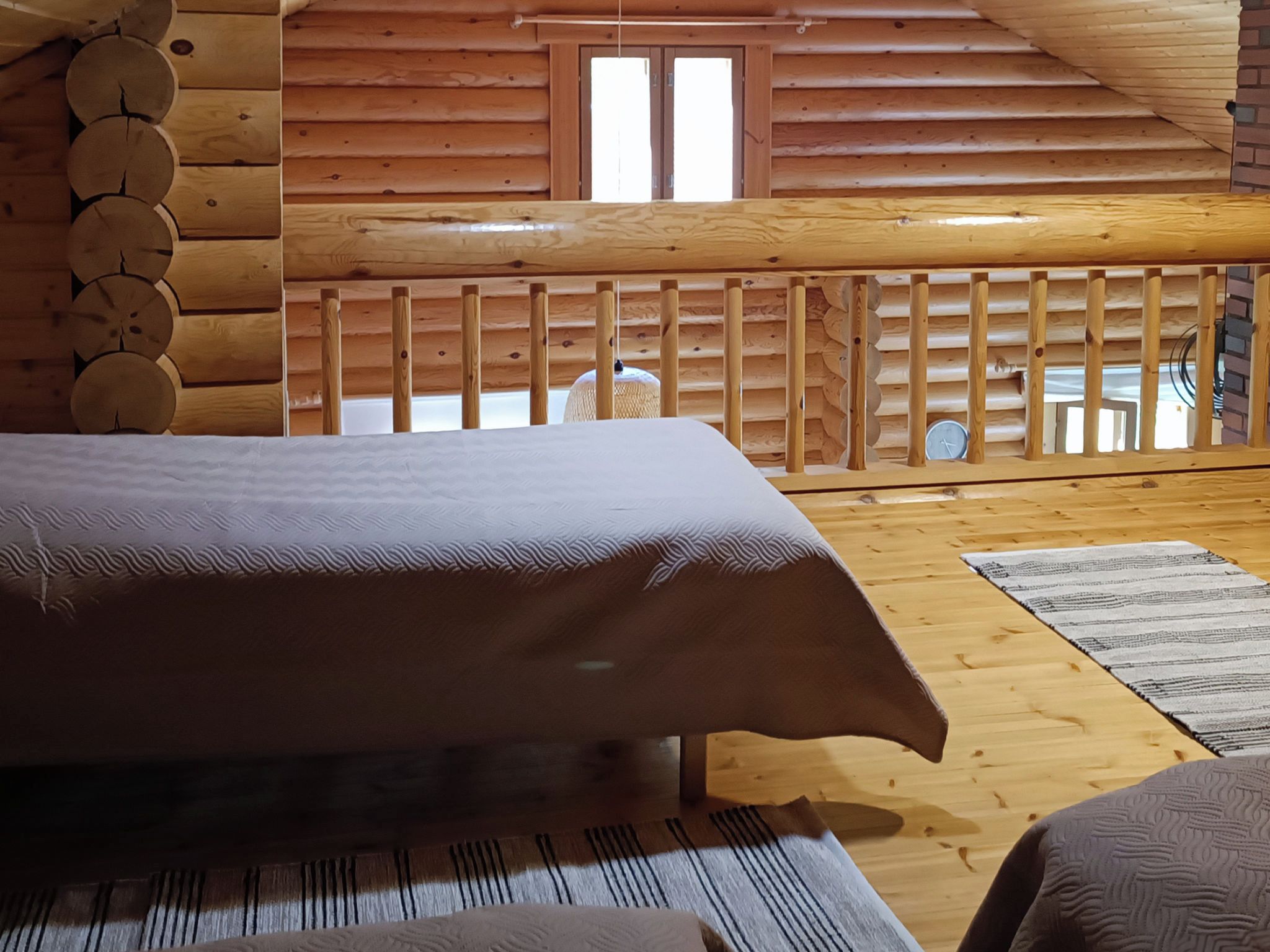 A wooden cabin interior with a bed, a window, and a wooden railing.
