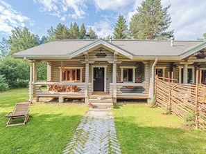 A log cabin with a porch, a wooden deck, and a stone pathway leading to the entrance.