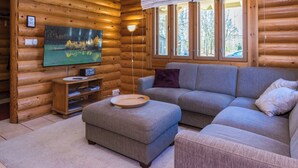 A log cabin interior with a television, sofa, ottoman, and a window with a view of trees. - Purnutar b by Interhome (Lieksa)