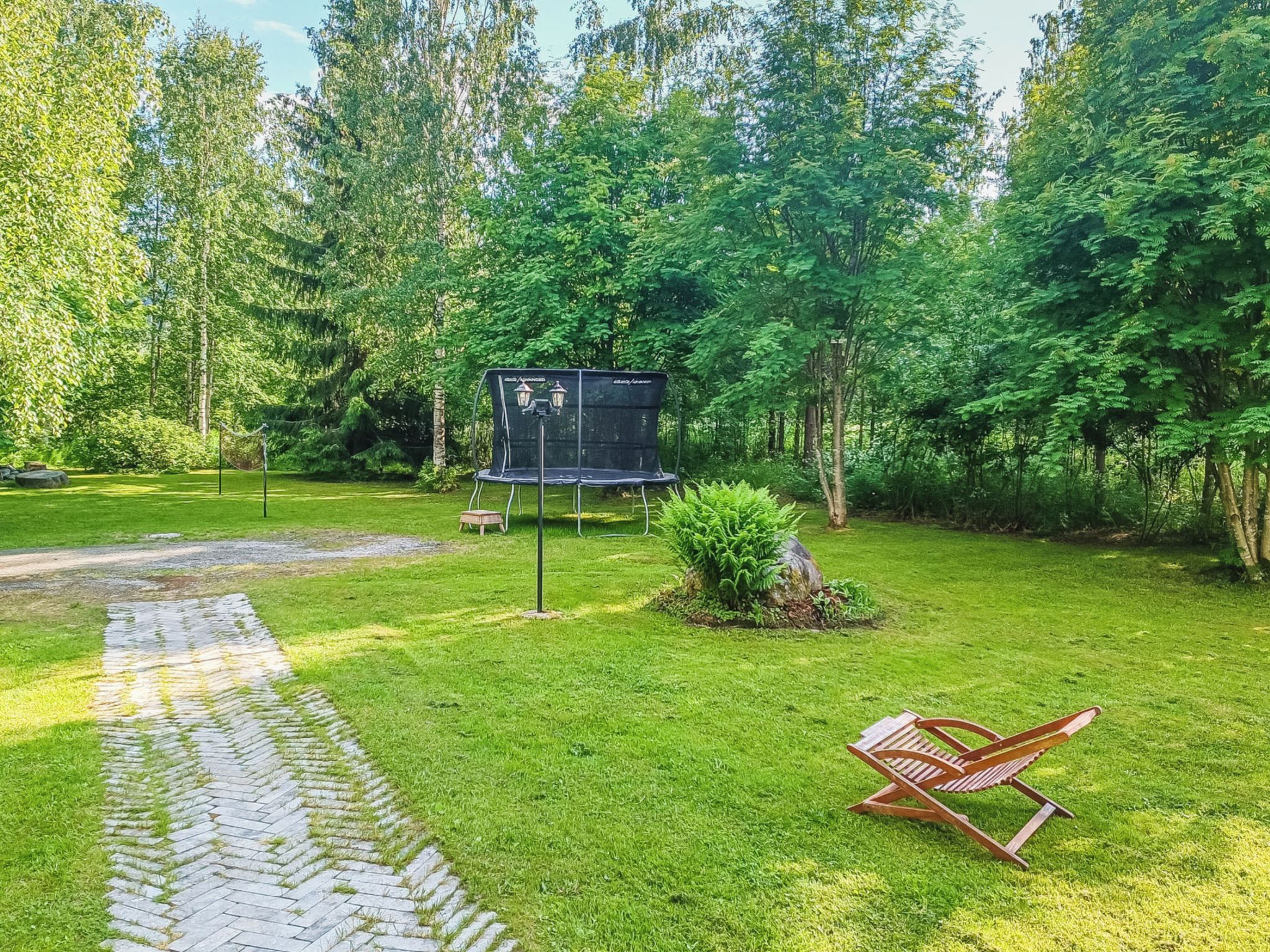 Ein Garten mit Trampolin, Schaukel und einem gepflasterten Weg.